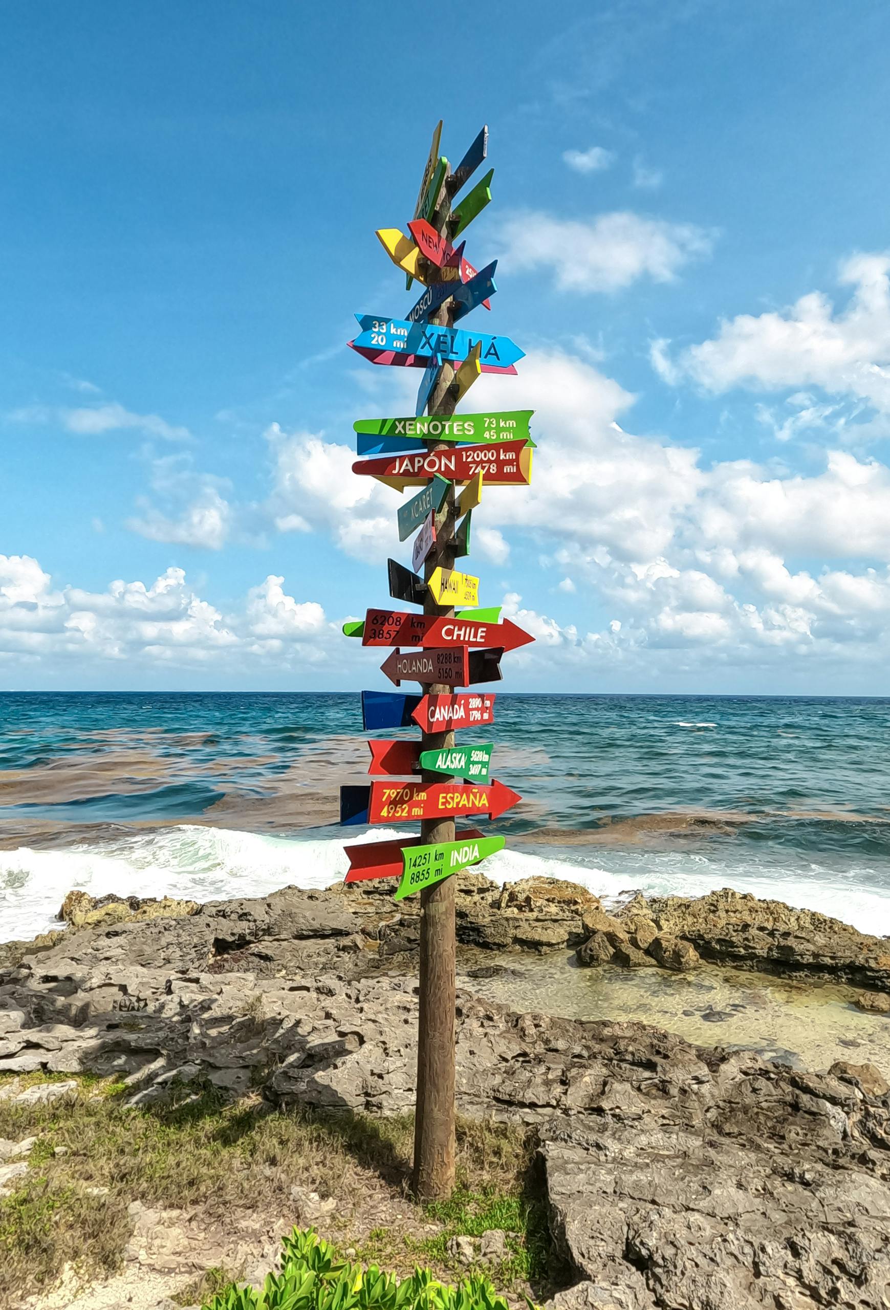 Vibrant signpost with directions to countries, located on a rocky beach in Tulum, Mexico.